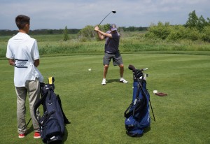 A student caddie watches a golfer's drive.